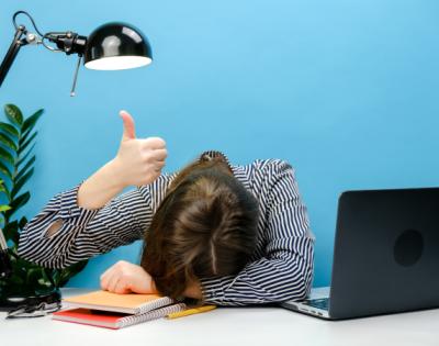 Tired exhausted woman in shirt sitting work sleep laid her head down on office desk with laptop show thumb up gesture ironically